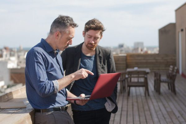 Two business man outside on a balcony, looking at a report