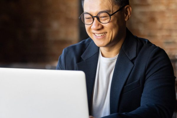 Asian man, smiling, working on a laptop