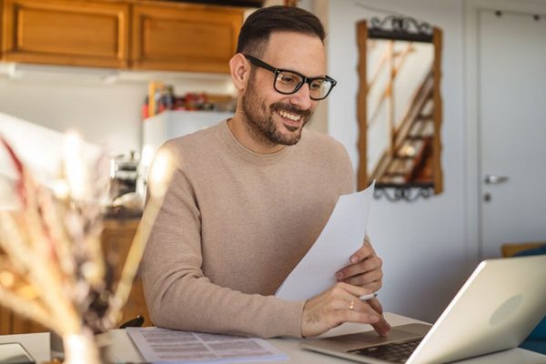 Man working on his laptop sitting on his desk, smiling.