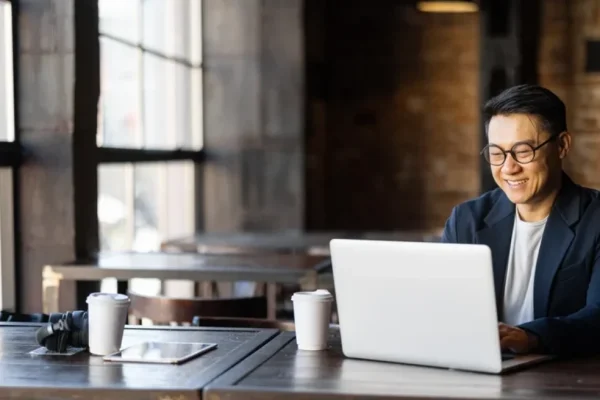 A smiling business man, sitting at a desk, working on his laptop