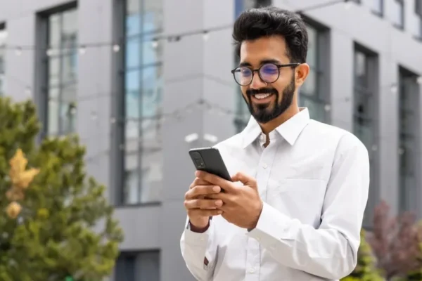 Business man using his phone, smiling, standing outside out on the street