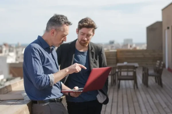 Two business man outside on a balcony, looking at a report