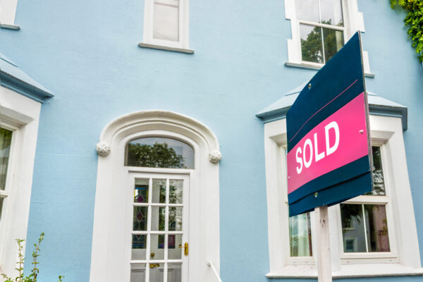 Estate agent sold sign in front of a beautiful blue house